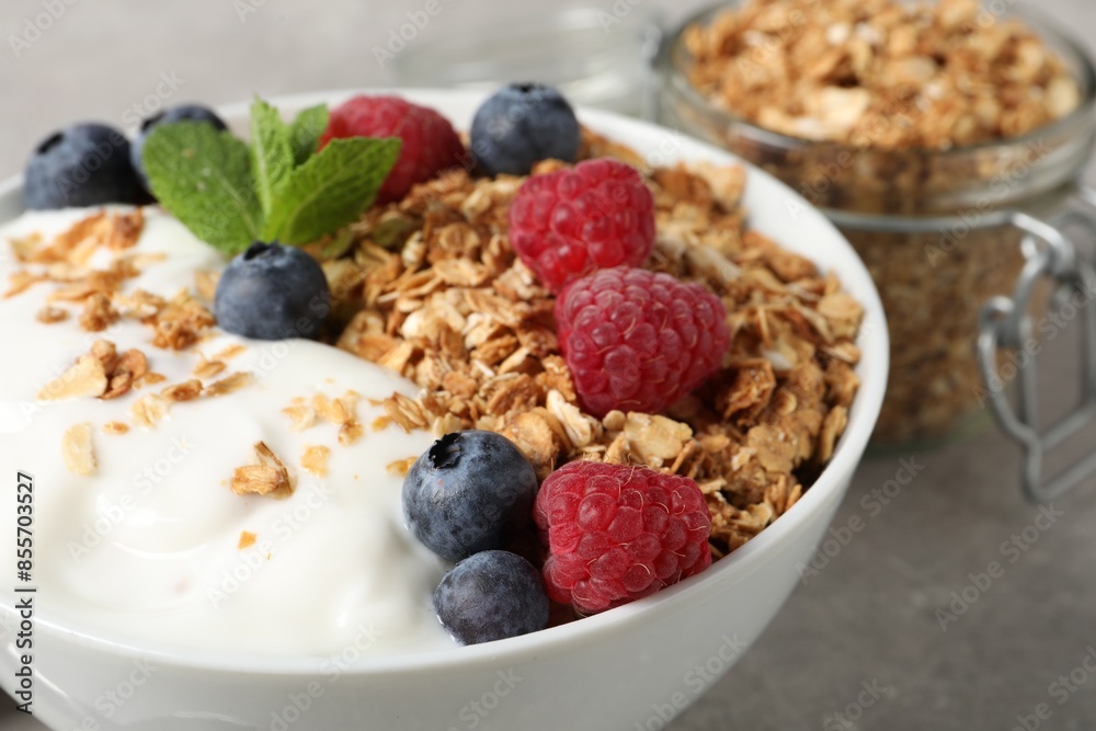 Tasty granola with berries and yogurt in bowl on grey textured table, closeup Tasty granola with berries and yogurt in bowl on grey textured table, closeup