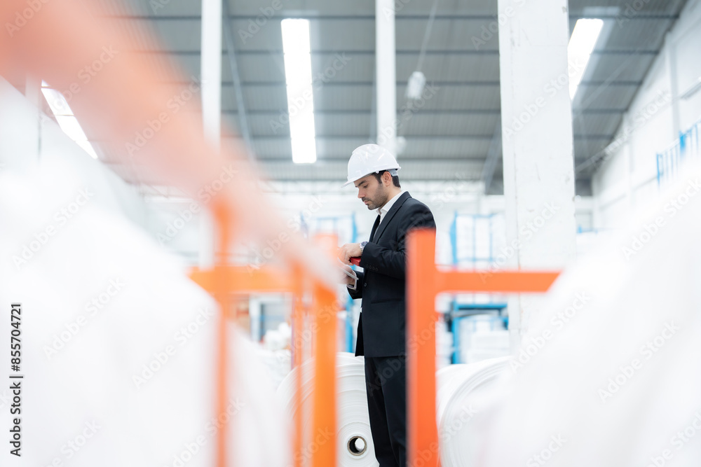 An American male engineer is reviewing an export manifest as an industrial automation solution deployed in a factory, seamlessly integrating into existing operations to increase efficiency.