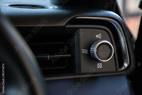 Close up of a modern car air conditioning mode button used to adjust the level of air inside the car or change the mode of the air conditioner in a modern dark black tone.