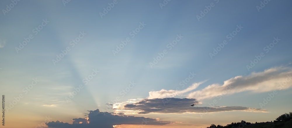 The red-orange evening sky. The rays of the sun pass through the clouds at sunset. A kite in the evening sun.