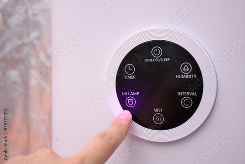 Close up hand pressing digital UV lamp button on smart humidifier in green house and smart home.