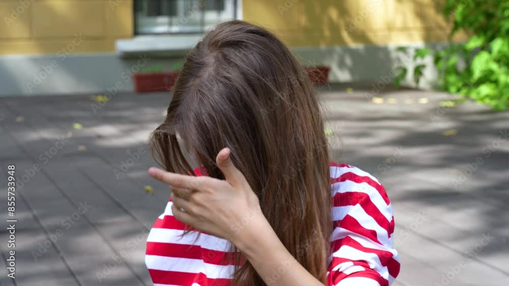 A young girl with long brown hair is fixing her hair while sitting outdoors on a summer day