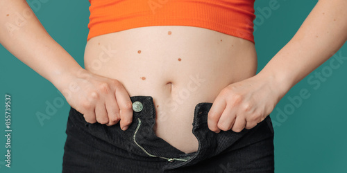 a close-up of the belly of an overweight woman, on which clothes do not fit, on a colored background. The concept of a healthy body, body positive. Panoramic banner.