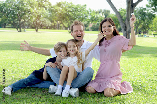 Wallpaper Mural Happy family sitting on green grass and waving hands at park, smiling father, mother, son and daughter spending time together outdoors in beautiful garden on holiday. Parents and kids have fun outside Torontodigital.ca