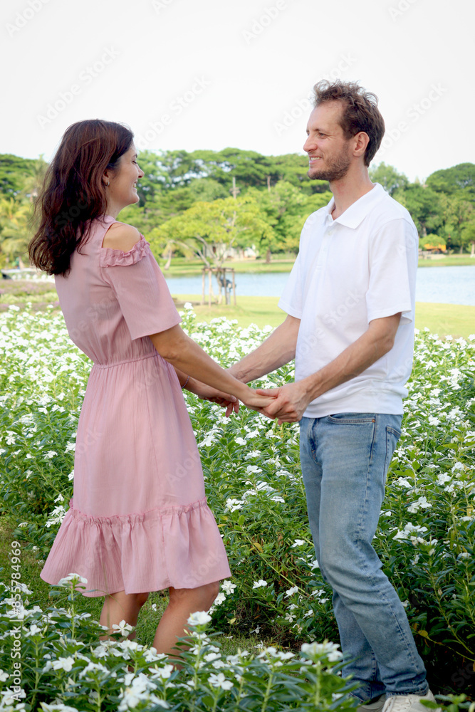 Happy beautiful couple enjoy spending time together outside at blooming flower garden. Joyful lover relaxing and walking around at park. Woman and man having romantic date outdoor on sunny day. Happy beautiful couple enjoy spending time together outside at blooming flower garden. Joyful lover relaxing and walking around at park. Woman and man having romantic date outdoor on sunny day.