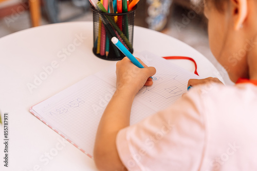 Принти на полотні A girl draws with a felt-tip pen with her left hand in a notepad on a white table