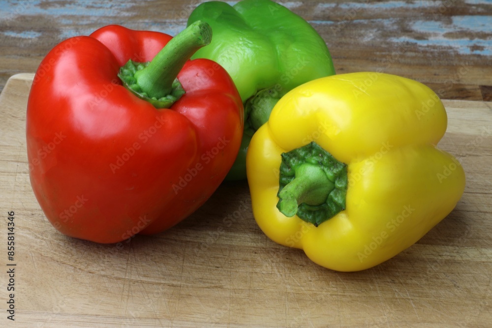 Fresh red, green, and yellow bell peppers on a wooden cutting board