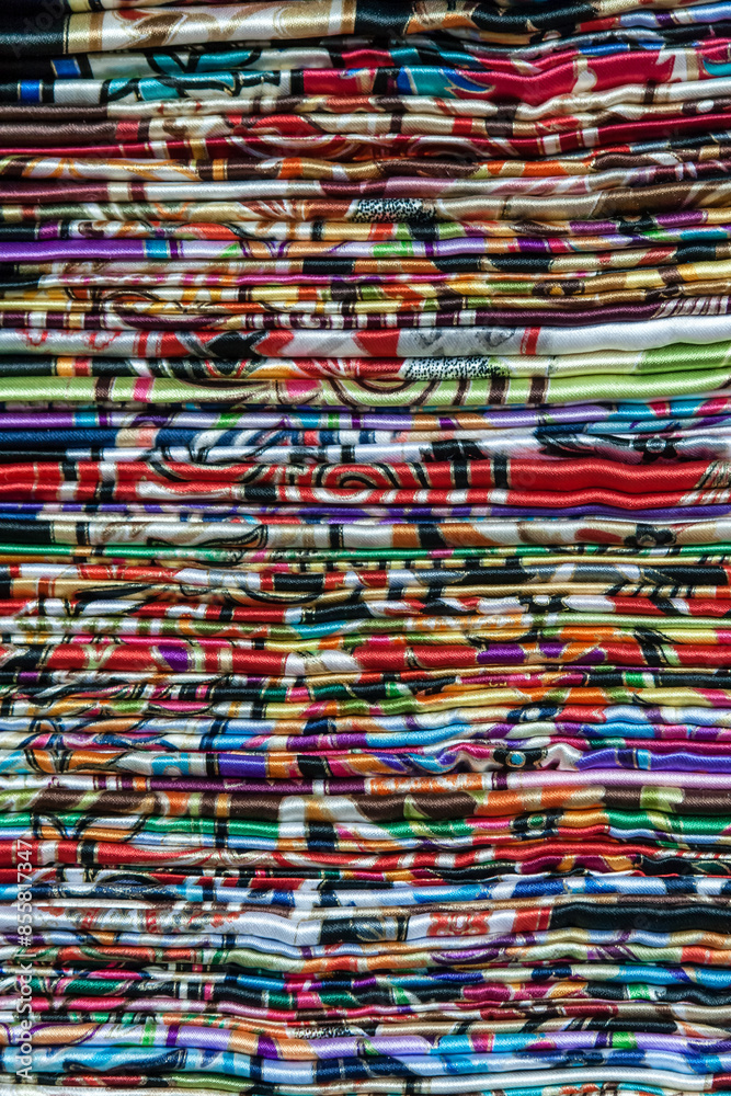 Stack of colorful, patterned fabrics, traditional shawls, arranged in layers in a local market, featuring various designs and vibrant colors, creating a visually striking and textured appearance. Stack of colorful, patterned fabrics, traditional shawls, arranged in layers in a local market, featuring various designs and vibrant colors, creating a visually striking and textured appearance.