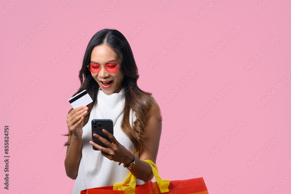 Shocked woman with shopping bag and credit card looking at mobile phone receiving discount and promotion online Shocked woman with shopping bag and credit card looking at mobile phone receiving discount and promotion online