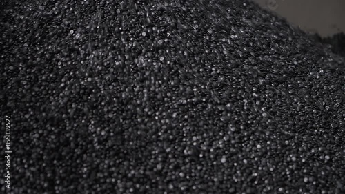 Huge amounts of black plastic material pellets piling up in the container. Piling lots of small recycled plastic pellets. Pouring the repurposed plastic pellets into the pile. Production process.