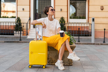 stylish woman traveling with yellow suitcase in Europe