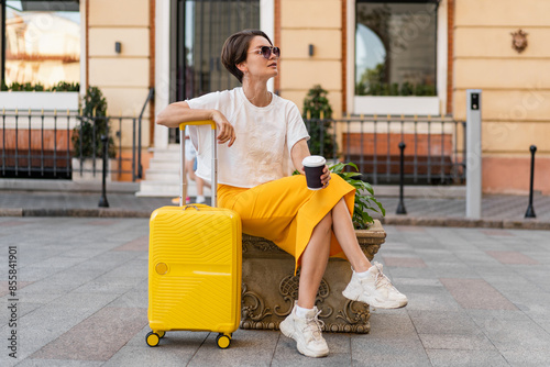 stylish woman traveling with yellow suitcase in Europe