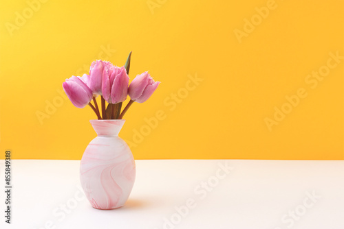 Vase with bouquet of pink tulip flowers in front of yellow background. Tenderness spring composition.