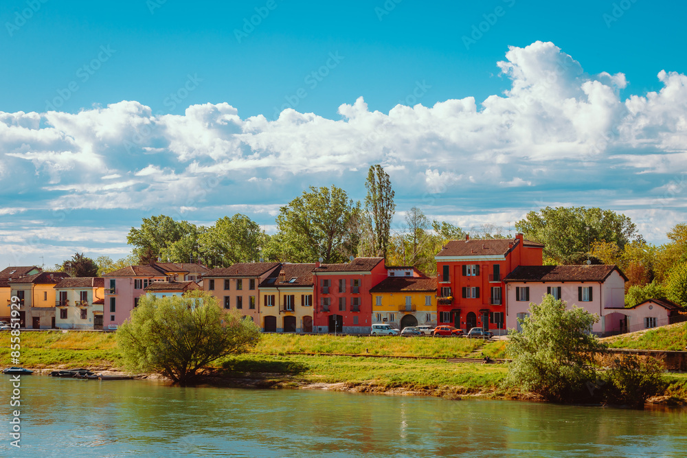 Fototapeta premium Colorful houses in front of the Ticino River running through the city of Pavia with white clouds in the background