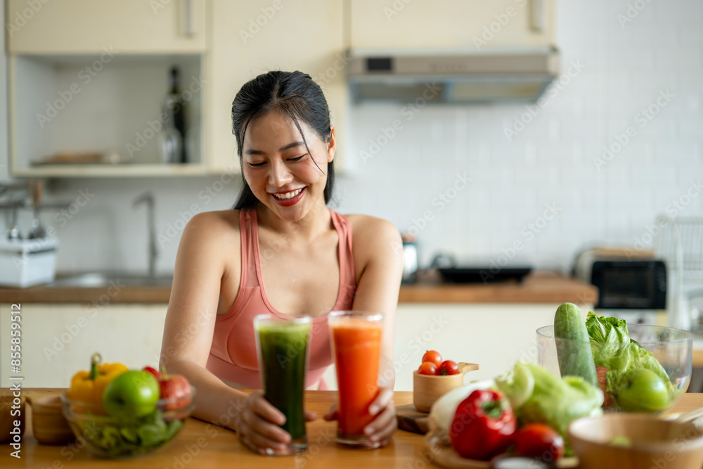A woman is smiling while holding two glasses of juice on a table with a variety A woman is smiling while holding two glasses of juice on a table with a variety