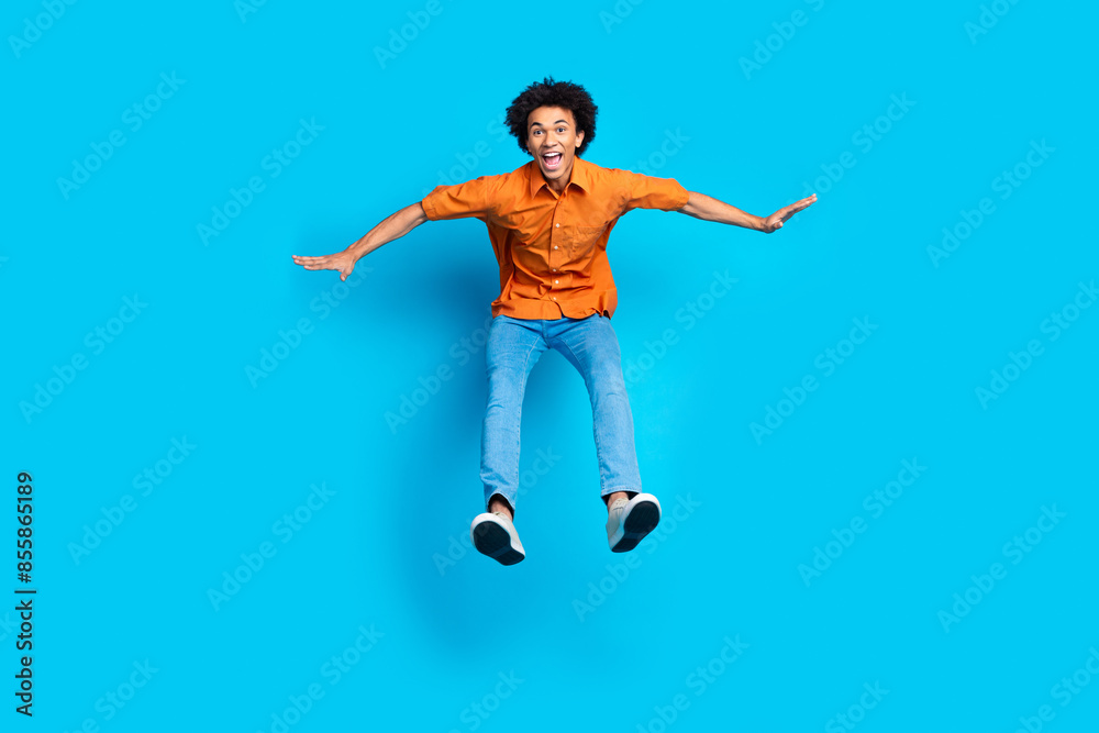 Full length photo of impressed positive guy dressed orange shirt jumping high empty space isolated blue color background Full length photo of impressed positive guy dressed orange shirt jumping high empty space isolated blue color background