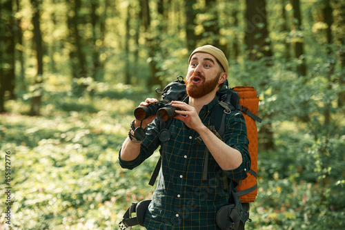 Discovering new place with binoculars. Bearded man is in the forest at daytime © standret
