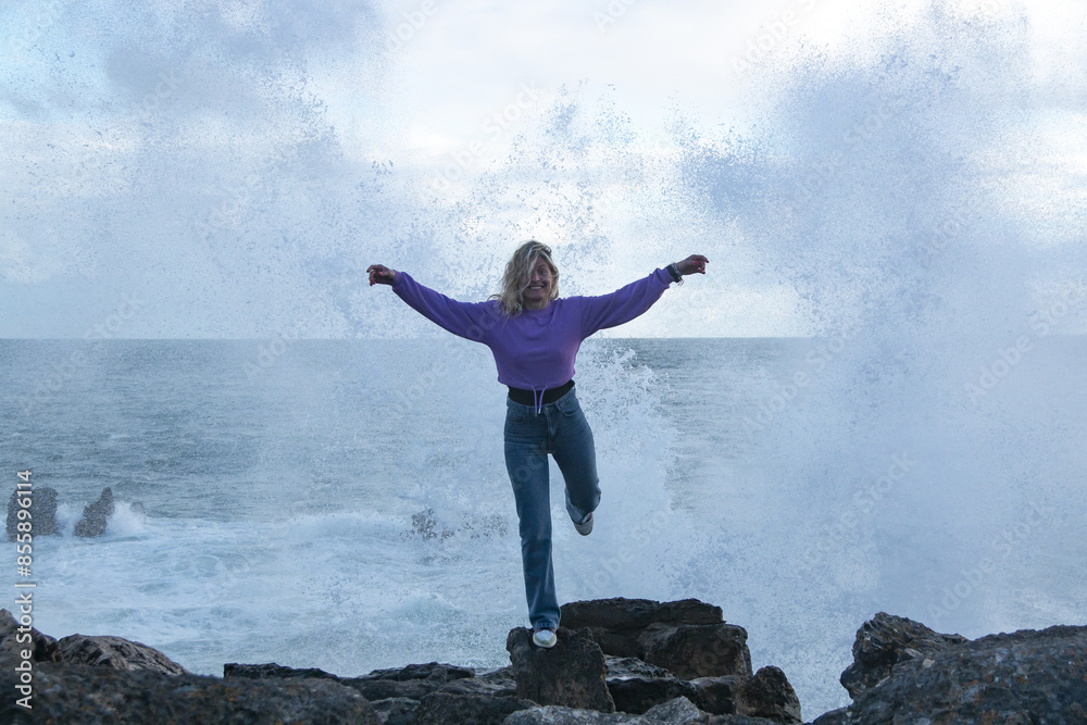 Blonde woman with the sea in the background and a wave breaking behind her during sunset Blonde woman with the sea in the background and a wave breaking behind her during sunset