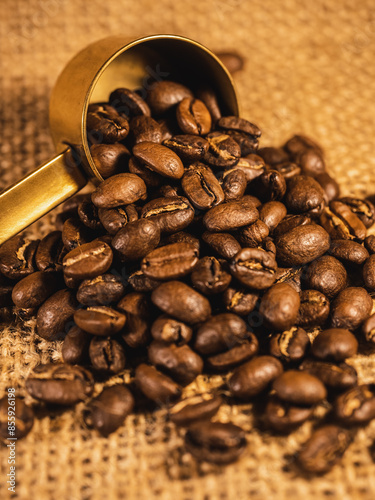 Coffee beans with gold measuring spoon on linen texture background	
