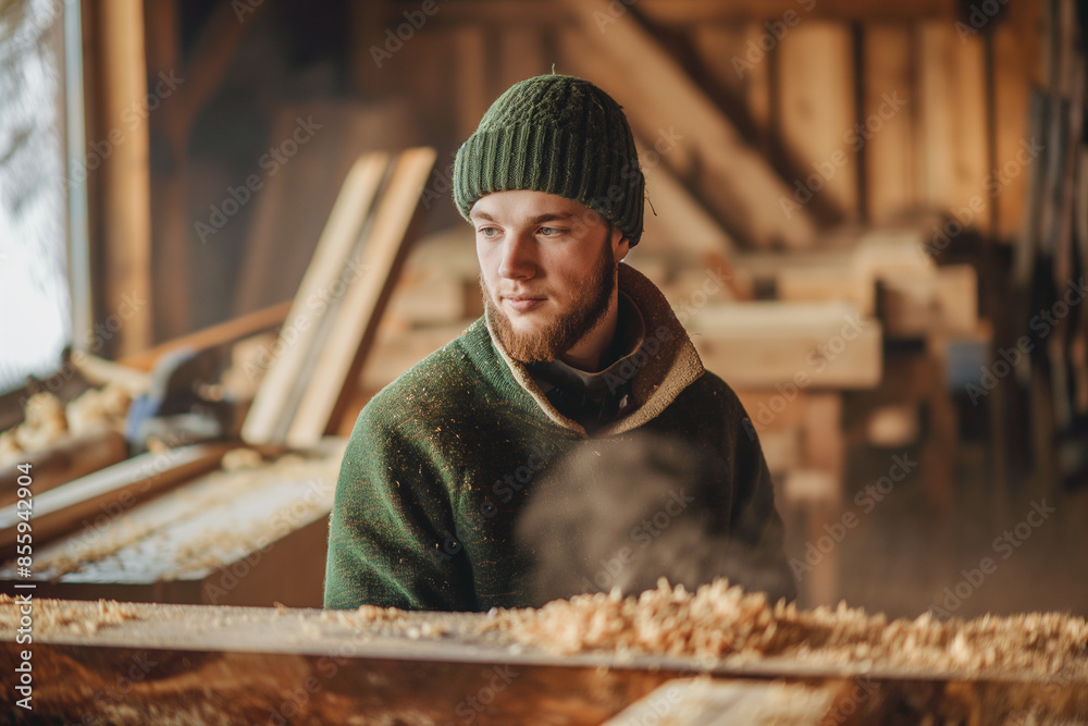 A man wearing a green hat and a green sweater sits in a wood shop A man wearing a green hat and a green sweater sits in a wood shop