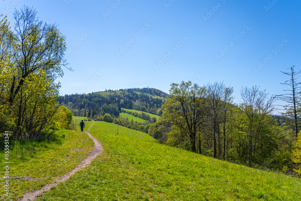A hiker strolls a path towards Kozakov Mountain in Bohemian Paradise, Czechia, enjoying views of rolling hills and lush forests along the way. A hiker strolls a path towards Kozakov Mountain in Bohemian Paradise, Czechia, enjoying views of rolling hills and lush forests along the way.