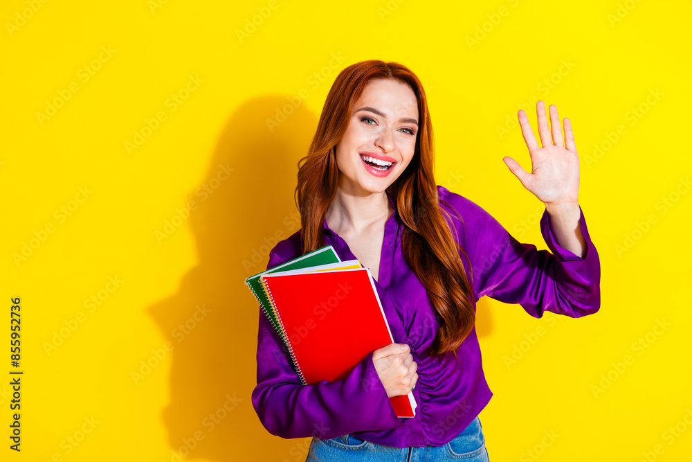 Photo portrait of attractive young woman hold copybooks wave hand dressed stylish violet clothes isolated on yellow color background Photo portrait of attractive young woman hold copybooks wave hand dressed stylish violet clothes isolated on yellow color background
