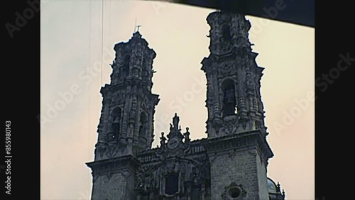 TAXCO DE ALARCON, MEXICO - circa 1970: Mexican peope and vintage cars on the square of the Church of Santa Prisca with bell towers. Archival of Mexico in South America in 1970s. photo