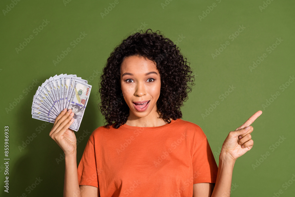 Photo portrait of attractive young woman hold money point empty space dressed stylish orange clothes isolated on khaki color background Photo portrait of attractive young woman hold money point empty space dressed stylish orange clothes isolated on khaki color background