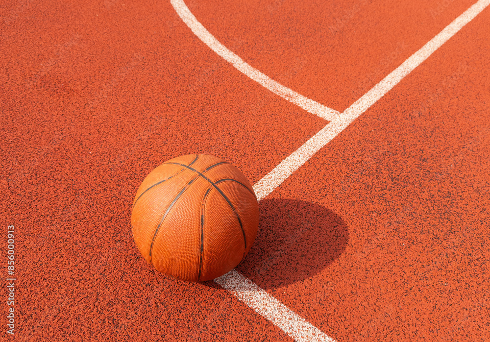 Basketball ball on the ground. Close-up ball on the red court. Basketball on the street or indoor court. Sports gear without people. Minimalism. Template, sport background Basketball ball on the ground. Close-up ball on the red court. Basketball on the street or indoor court. Sports gear without people. Minimalism. Template, sport background