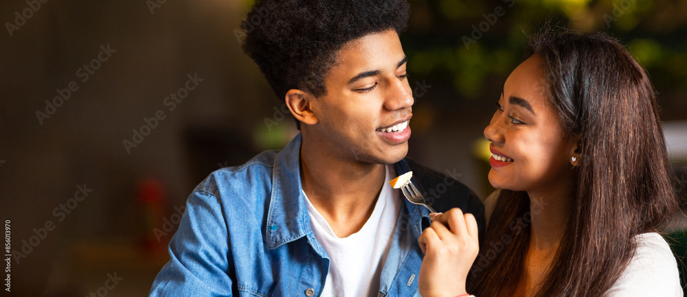 Naklejka premium African American guy and girl are standing close, smiling warmly at each other. They appear happy and engaged in a pleasant conversation, panorama with copy space