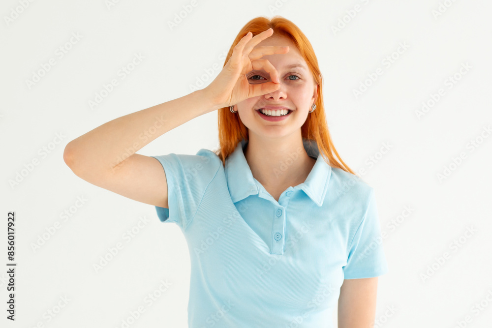 Fototapeta premium Beautiful young woman wearing casual blue t-shirt doing ok gesture with hand smiling, eye looking through fingers with happy face.