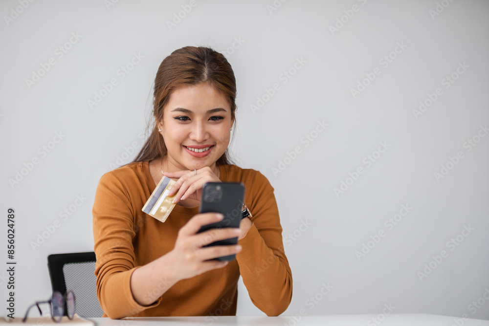 Woman Smiling While Using Credit Card and Smartphone for Online Shopping in a Modern Minimalist Setting Woman Smiling While Using Credit Card and Smartphone for Online Shopping in a Modern Minimalist Setting