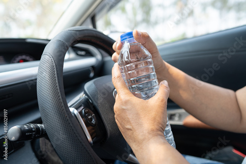Asian woman driver holding bottle for drink water while driving a car. Plastic hot water bottle cause fire.