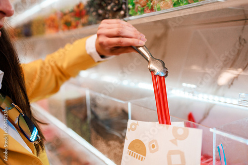 Unrecognizable woman hand picking strawberry bar liquorice in candy store.