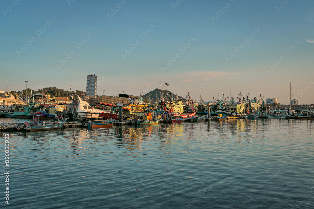 A panoramic view of a harbor filled with docked fishing boats, with the setting sun casting a warm glow on the water and boats. A panoramic view of a harbor filled with docked fishing boats, with the setting sun casting a warm glow on the water and boats.