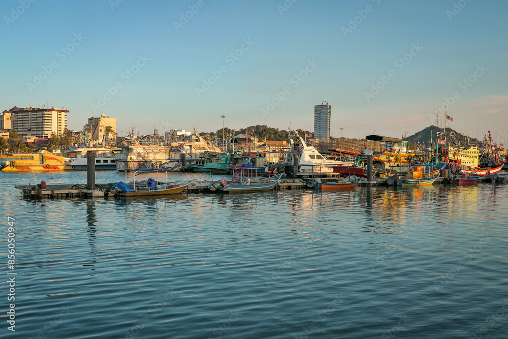 A panoramic view of a harbor filled with docked fishing boats, with the setting sun casting a warm glow on the water and boats. A panoramic view of a harbor filled with docked fishing boats, with the setting sun casting a warm glow on the water and boats.