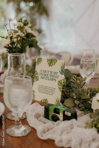 Table setting at a wedding with a disposable camera, flowers, and a sign encouraging guests photo