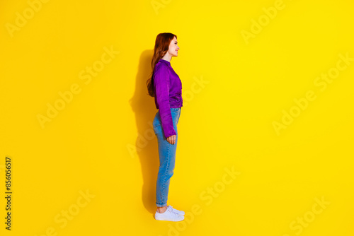 Side profile photo of beautiful foxy hair young girl in jeans and shirt looking billboard isolated on yellow color background