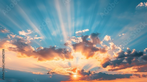 Hopeful sunrise nature background of dramatic blue sky and vibrant orange sun rays emerging from the clouds.