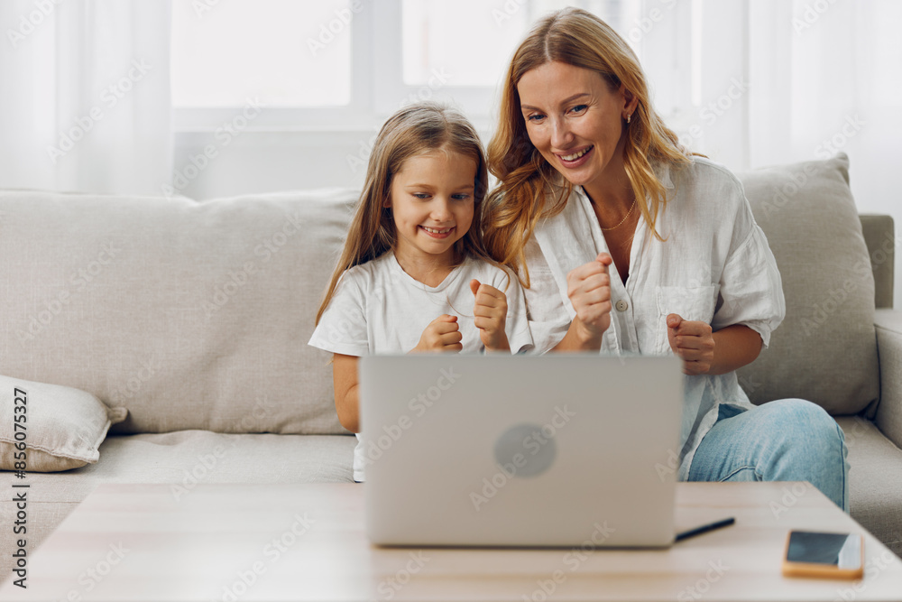 Mother and daughter bonding on the couch while browsing together on a laptop screen in a cozy living room Mother and daughter bonding on the couch while browsing together on a laptop screen in a cozy living room