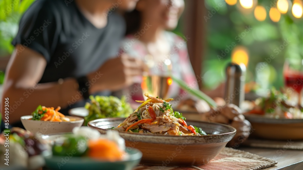 A dinner setting with various dishes on a table, blurred people in the background enjoying a meal. A dinner setting with various dishes on a table, blurred people in the background enjoying a meal.