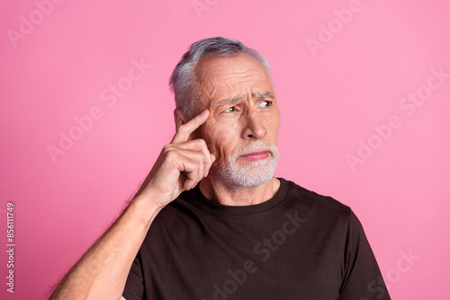 Portrait of minded man with white gray beard dressed brown t-shirt look empty space finger on head isolated on pink color background