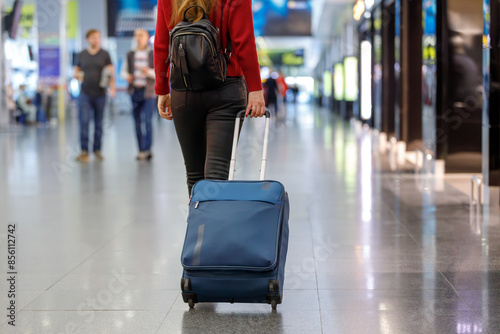Woman in Red Sweater and Black Jeans Pulling Suitcase through Airport