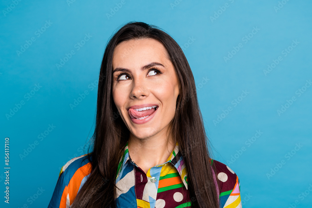 Fototapeta premium Photo of pretty young girl look interested empty space lick teeth wear trendy colorful print outfit isolated on blue color background