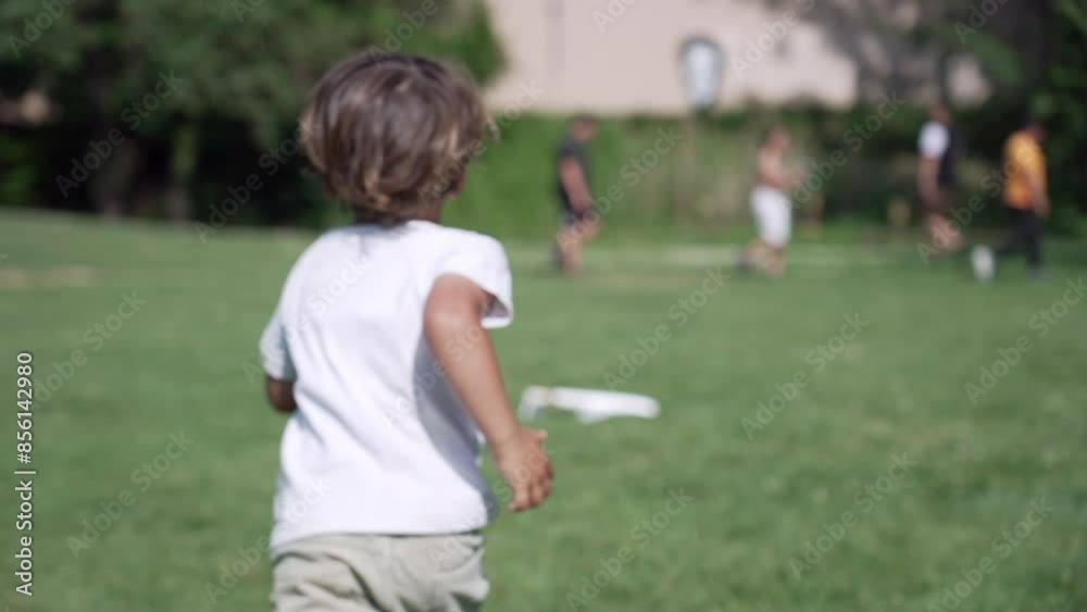 Child Runs Towards Toy Glider Across Park Grass, Getting Ready for Another Throw, Camera Captures his Back Child Runs Towards Toy Glider Across Park Grass, Getting Ready for Another Throw, Camera Captures his Back