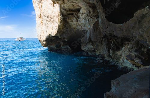 Fascinante vista de los acantilados y la entrada a la Cueva de Neptuno en Cabo Caccia, Cerdeña, Italia. Las imponentes paredes de roca caliza se alzan sobre el mar azul profundo.