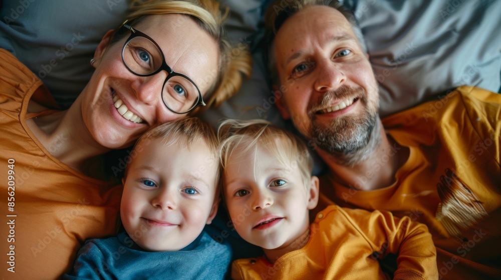 A joyful family of four smiling and cuddling together on a bed with two adorable children nestled between their parents all wearing matching orange tops. A joyful family of four smiling and cuddling together on a bed with two adorable children nestled between their parents all wearing matching orange tops.