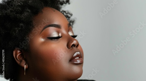 Elegant close-up of a woman with dark skin wearing subtle makeup including smoky eyeshadow eyeliner and nude lipstick with her head tilted down and her eyes closed