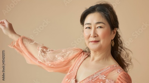 Woman in pink floral-embellished blouse smiling with hair swept to side arm raised in gesture against soft-focus beige background. photo