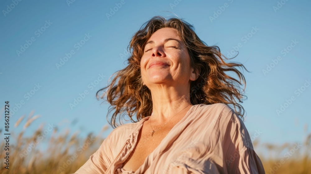 A woman with closed eyes smiling and her hair blowing in the wind standing in a field with a blue sky background. A woman with closed eyes smiling and her hair blowing in the wind standing in a field with a blue sky background.